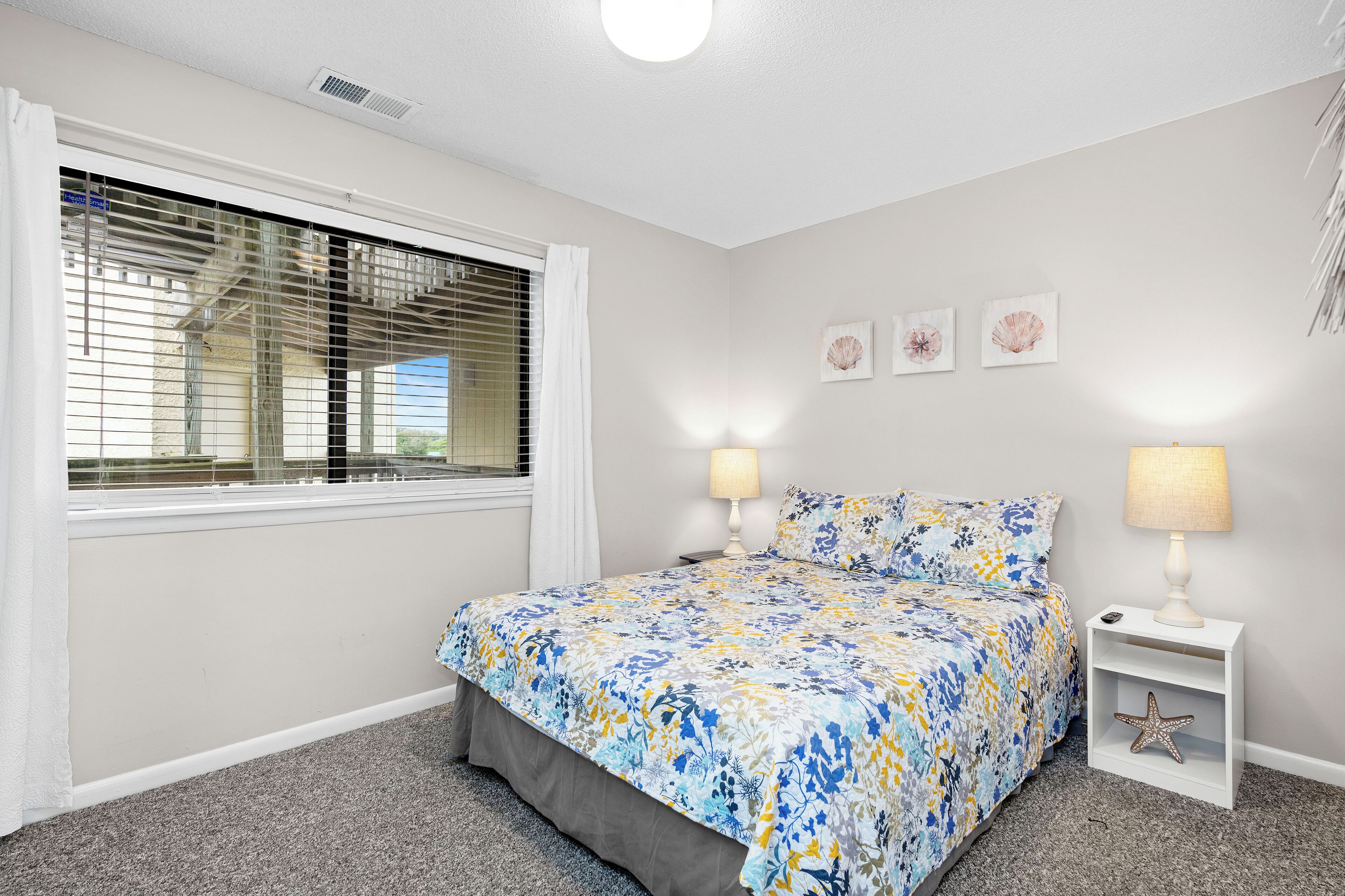 A bedroom with a bed, two bedside lamps, a starfish decoration, and a window with blinds.