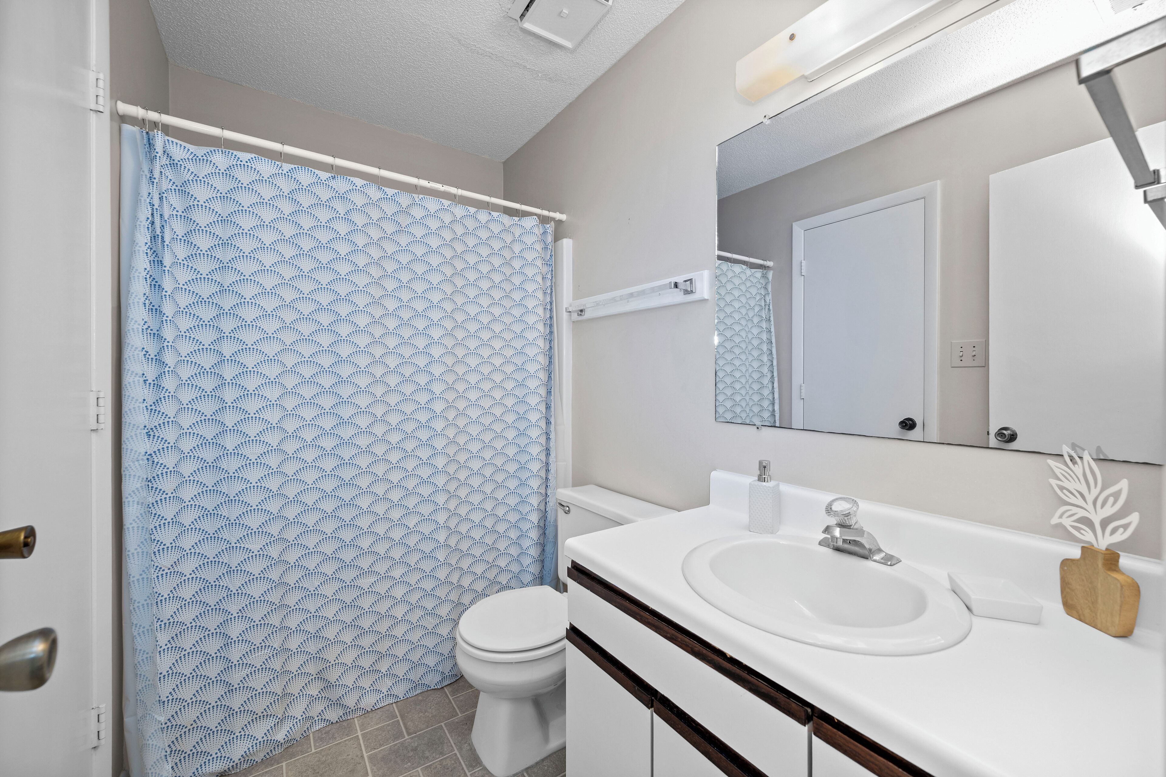 A bathroom with a shower curtain, toilet, sink, and mirror.