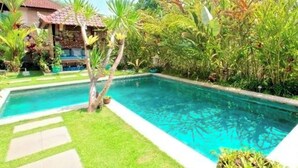 Ein Pool, umgeben von üppiger Vegetation und einem Gebäude mit Ziegeldach.