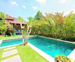 Une piscine entourée d’une végétation luxuriante et un bâtiment doté d’un toit en tuiles.
