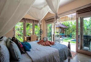 Une chambre à coucher avec un lit à baldaquin, un bureau et une vue sur un jardin luxuriant.
