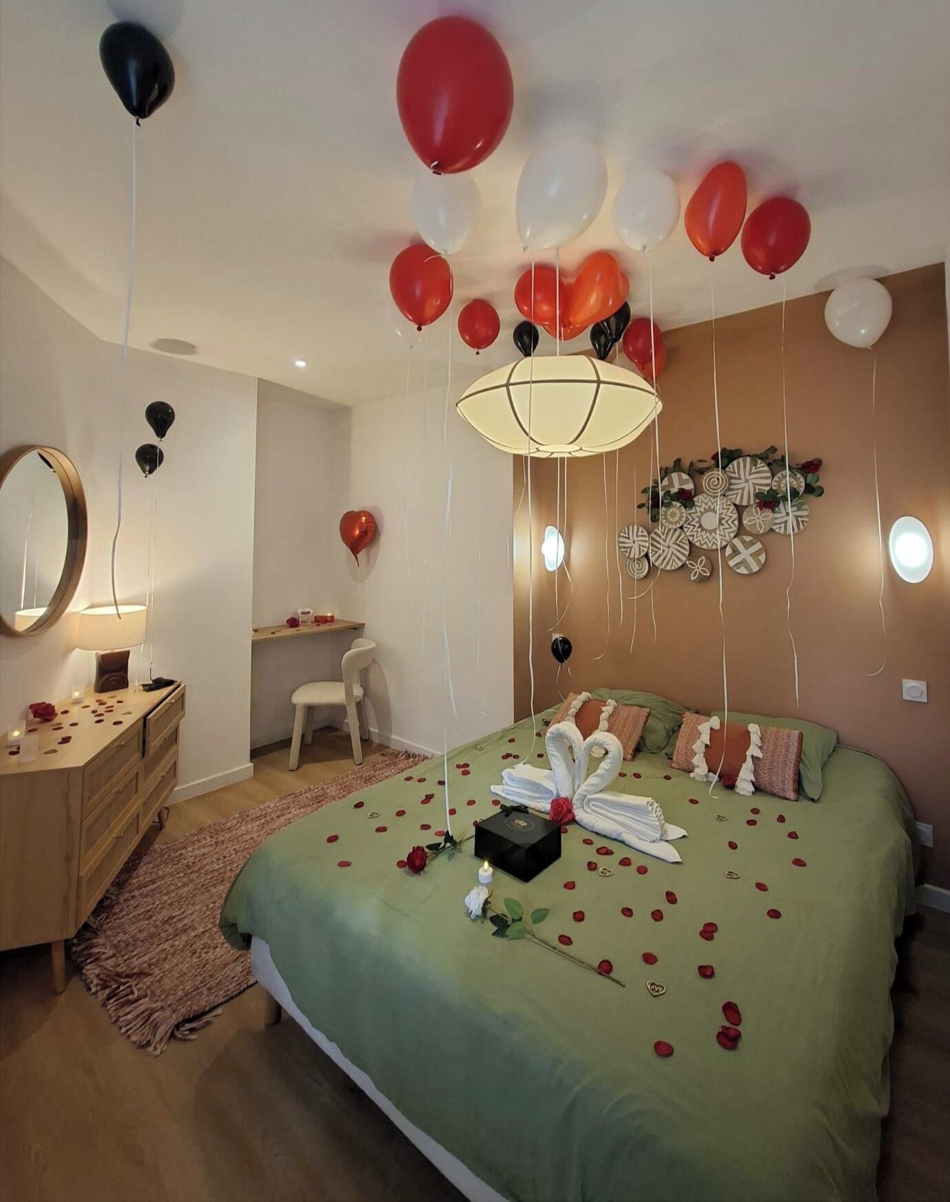 Un dormitorio con colcha verde, una mesita de noche con lámpara, un espejo y una pared decorada con platos.