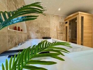 Et moderne badeværelse med et stort badekar, en træsauna og en hylde med toiletartikler.