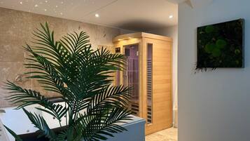 Une salle de spa agrémentée d’une grande plante, d’un sauna en bois et d’une œuvre d’art fixée au mur.