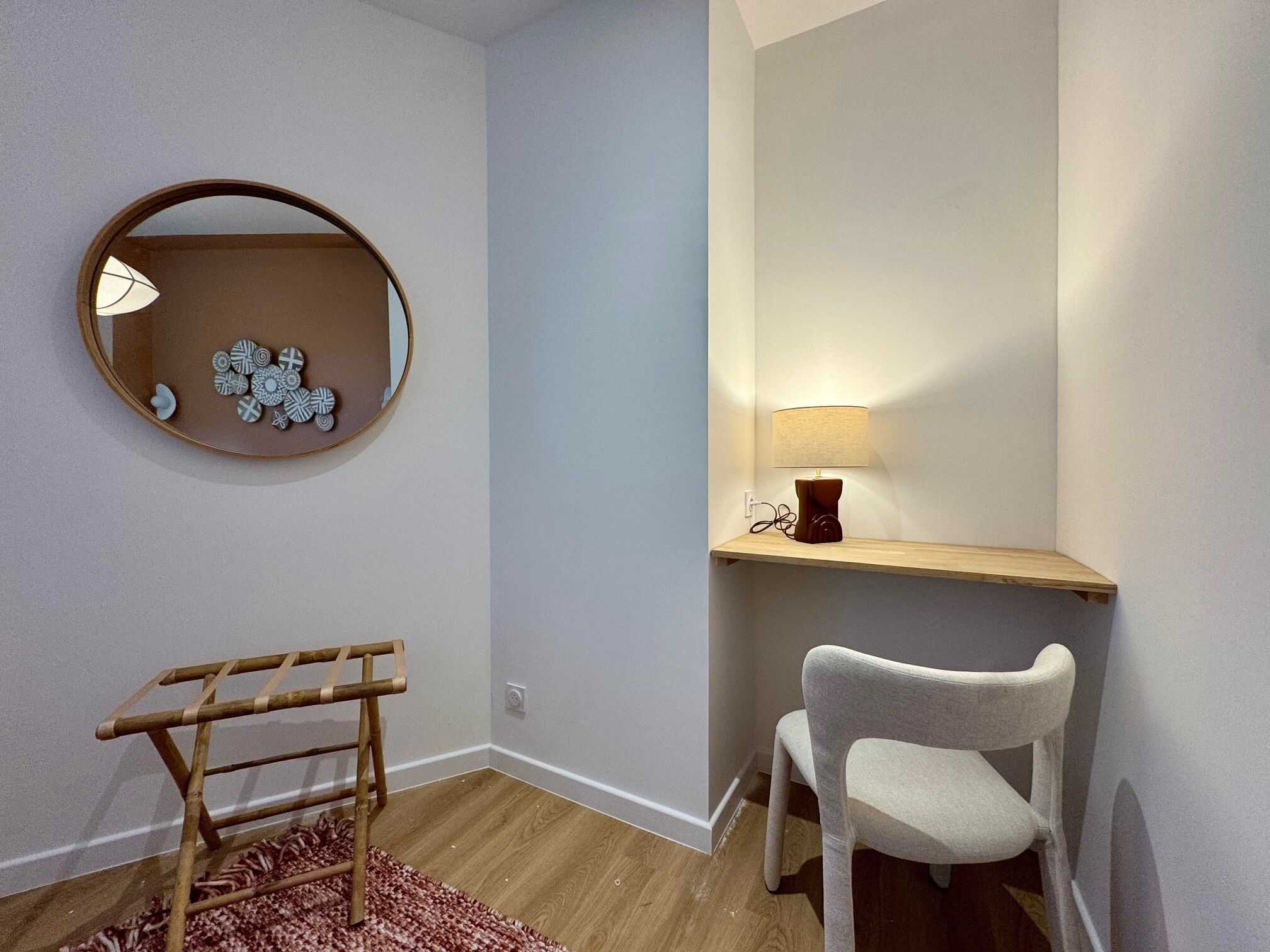 A corner room with a wooden chair, a small table with a lamp, a mirror with decorative items, and a wooden ladder.
