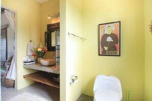 Ein Badezimmer mit Waschbecken, Spiegel und Toilette. An der Wand hängt ein gerahmtes Bild und auf dem Boden steht ein Korb.