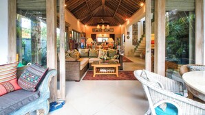 A spacious living area with a high ceiling, wicker furniture, and a central coffee table. - Hibiscus/Upper Suite/Ubud/Pool/AC (Bali)