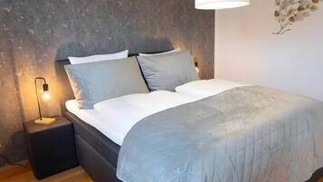 A bedroom with a bed, bedside tables, a hanging light fixture, and a textured wall.