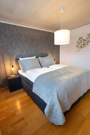 Un dormitorio con cama, mesitas de noche, una lámpara colgante y pared con textura.