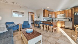 A modern kitchen with wooden cabinets, a stainless steel refrigerator, and a bar area with stools.