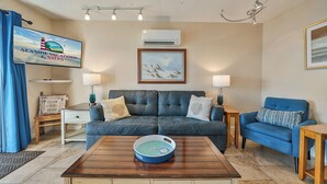 A living room with a dark blue sofa, a wooden coffee table, and a television displaying 'Seaside Vacations & Sales'.