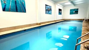 Ein Innenpool mit klarem Wasser, umgeben von weißen Wänden und einer Decke mit runden Leuchten.