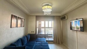 Ein Zimmer mit blauem Sofa, einem Chandelier, einem Fernseher und einem Balkon mit Tisch und Stühlen.