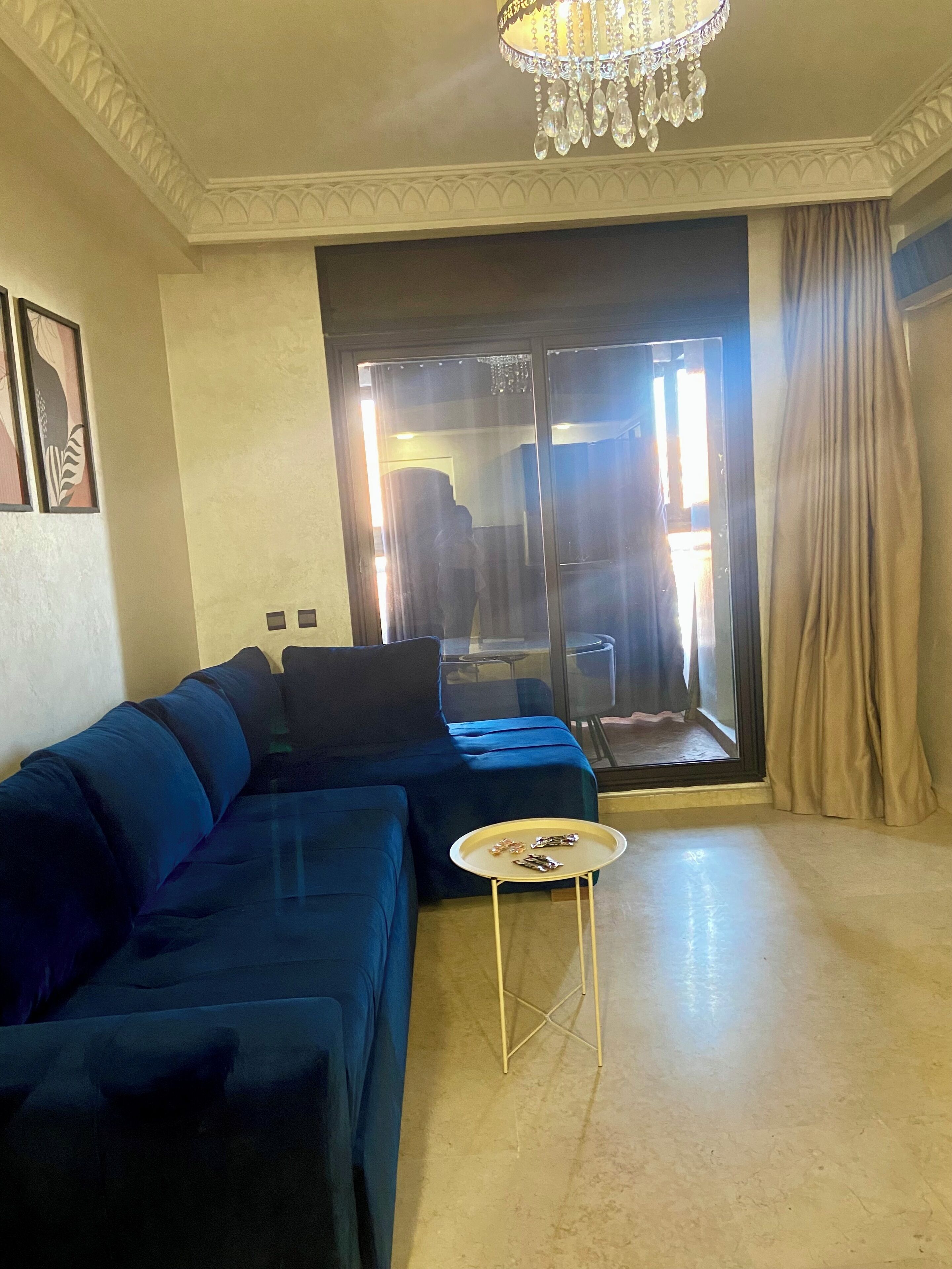 A living room with a dark blue sofa, a small white table, and a chandelier.