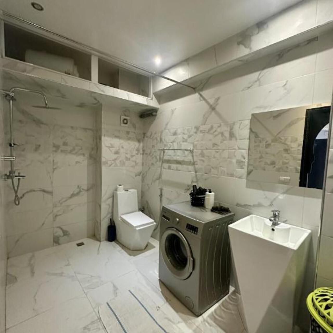 A modern bathroom with a shower, toilet, washing machine, and sink.