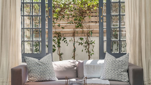 A cozy seating area with a cushioned sofa, a glass candle holder, and a view of a wooden trellis with climbing plants. - Bellevue House (Cape Town)