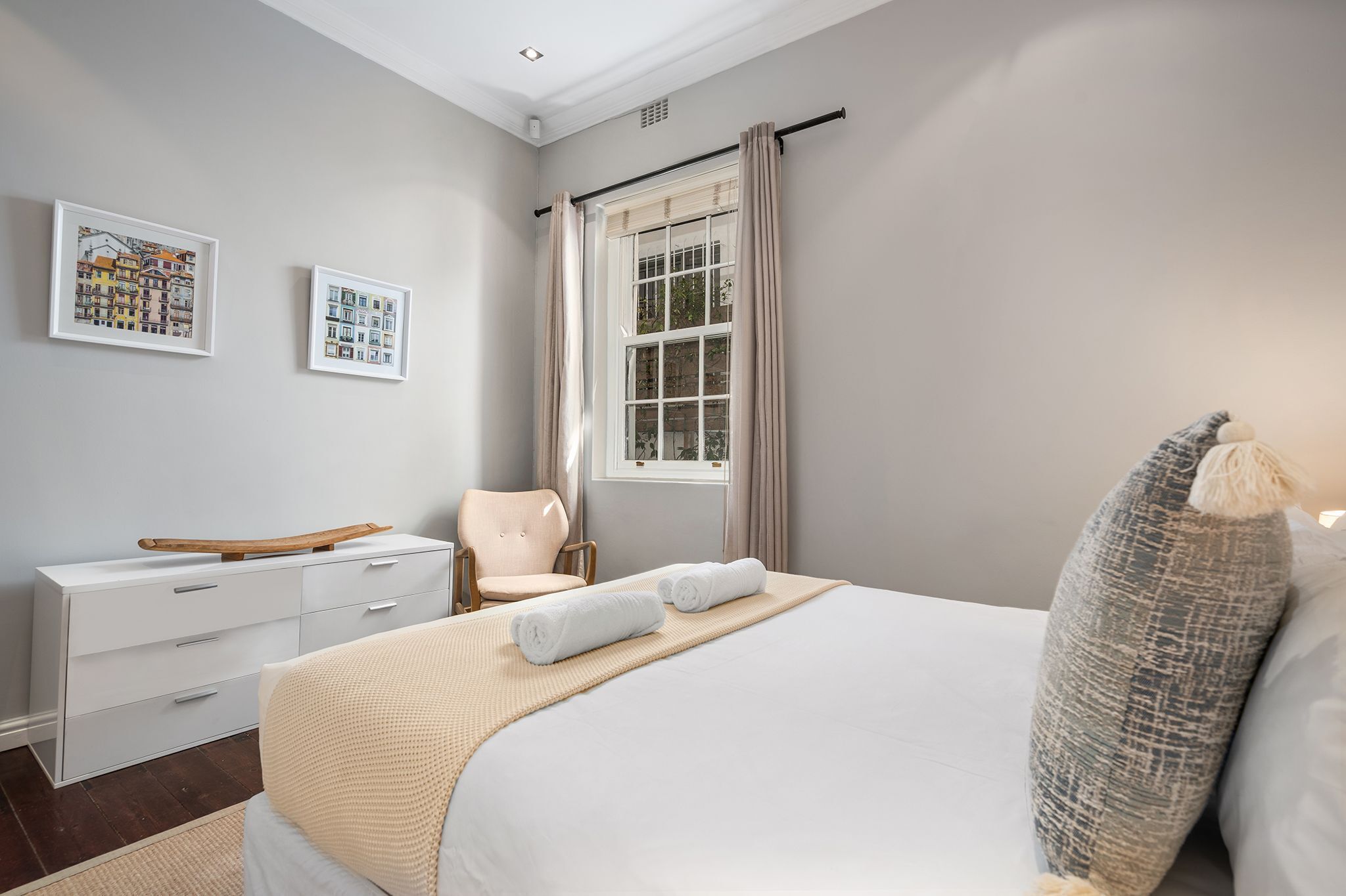 A bedroom with a bed, a chair, a dresser, and two framed pictures on the wall.