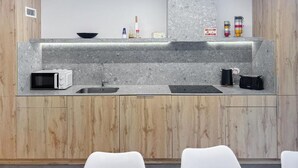 A modern kitchen with wooden cabinets, a granite countertop, a microwave, a sink, and a coffee maker. - Magnolia Suites & Stays (Porto)