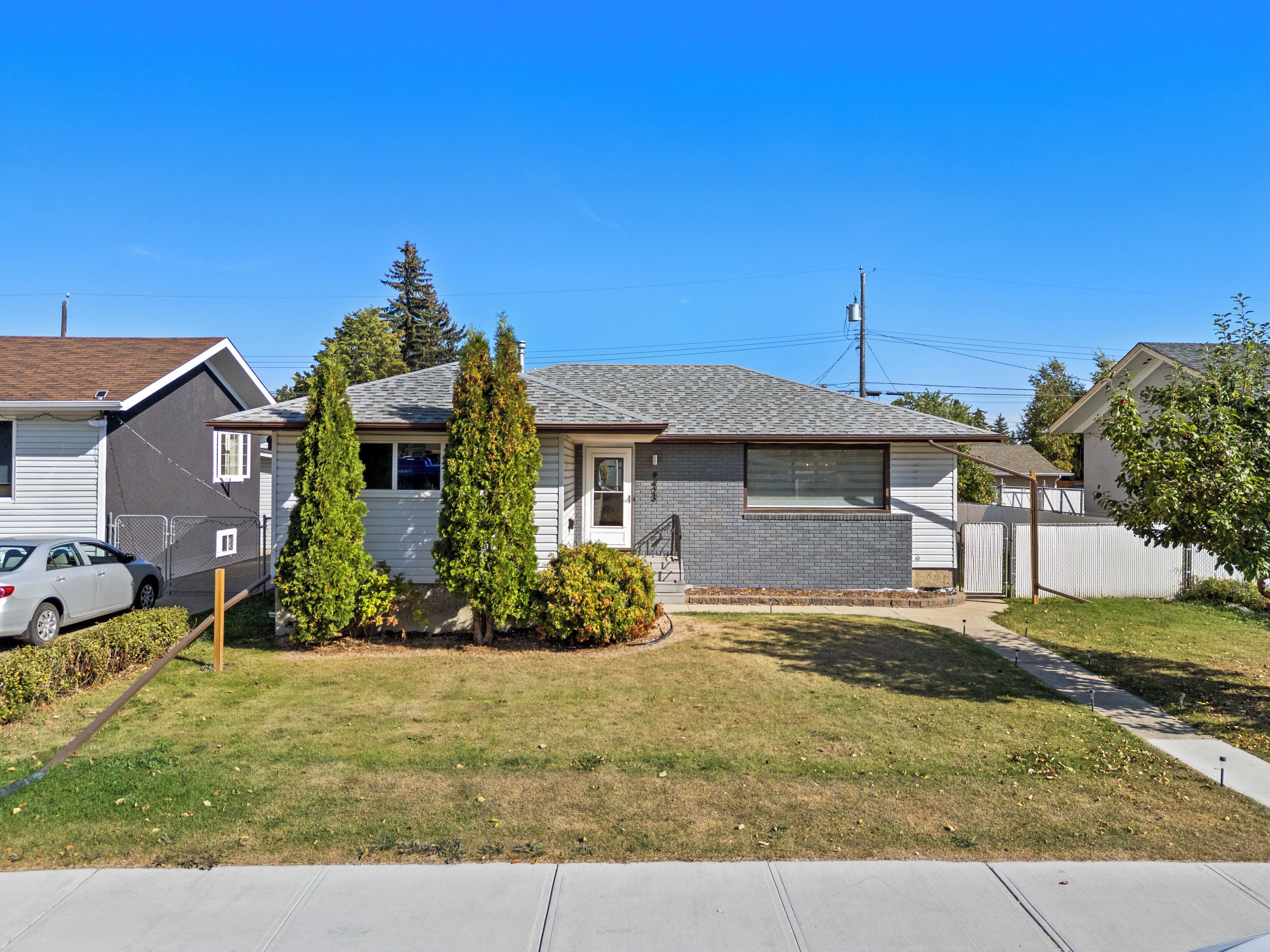 A single-story residential house with a front yard, a car parked in the driveway, and a neighboring house.