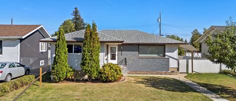 A single-story residential house with a front yard, a car parked in the driveway, and a neighboring house.