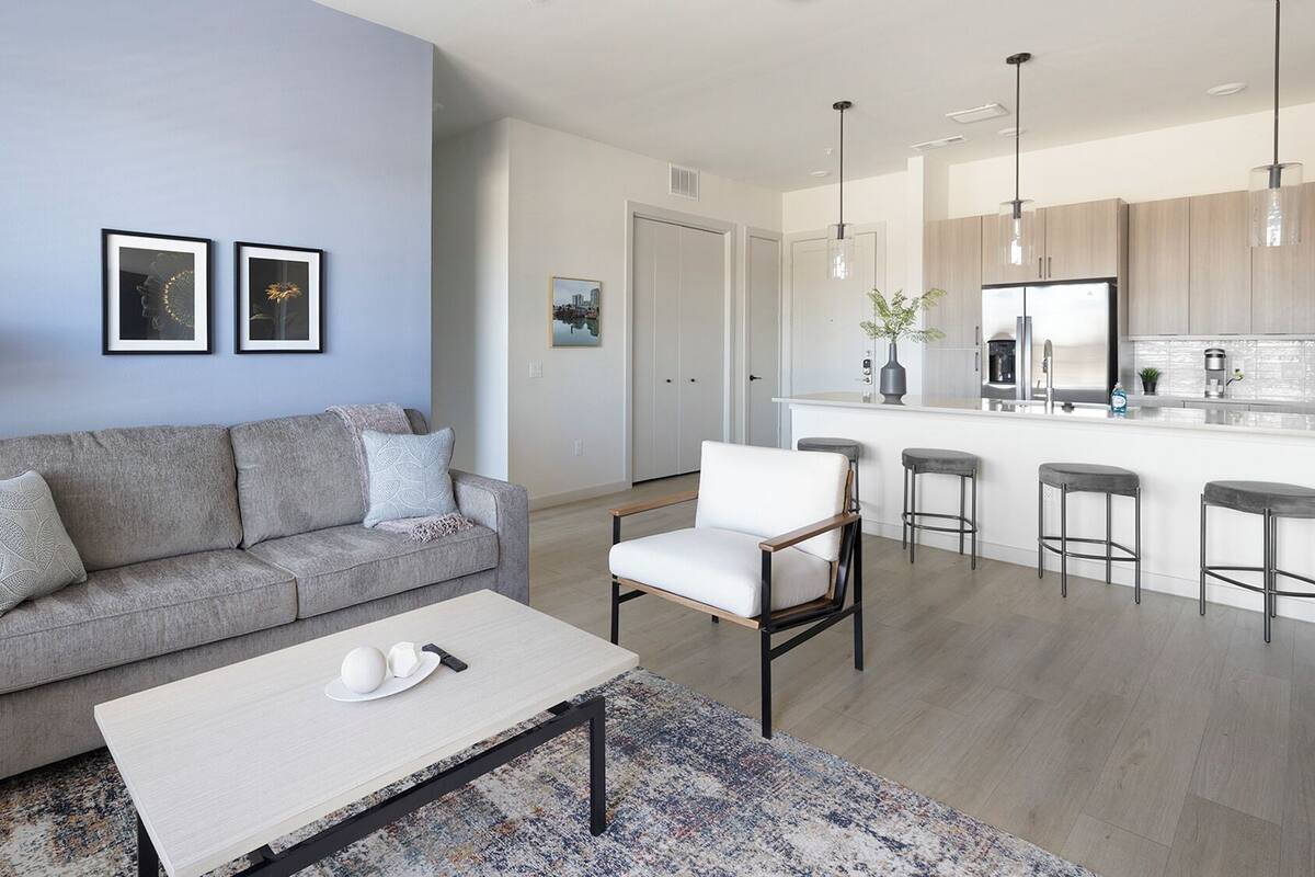 A modern living room with a sofa, coffee table, and a kitchen area with bar stools.