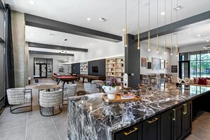 A modern kitchen with a marble island, black cabinets, and gold handles. There are bar stools and a pool table in the background. - Landing Furnished Apartments - Plano (Plano)
