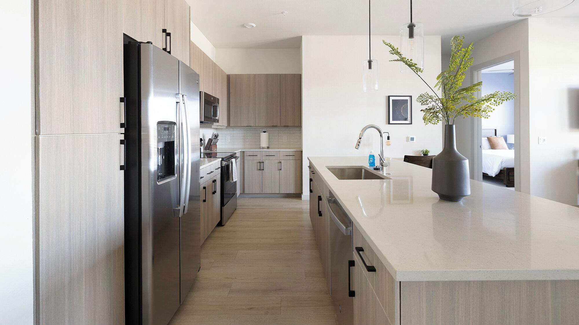 A modern kitchen with stainless steel appliances, wooden cabinets, a large island with a sink, and pendant lighting.