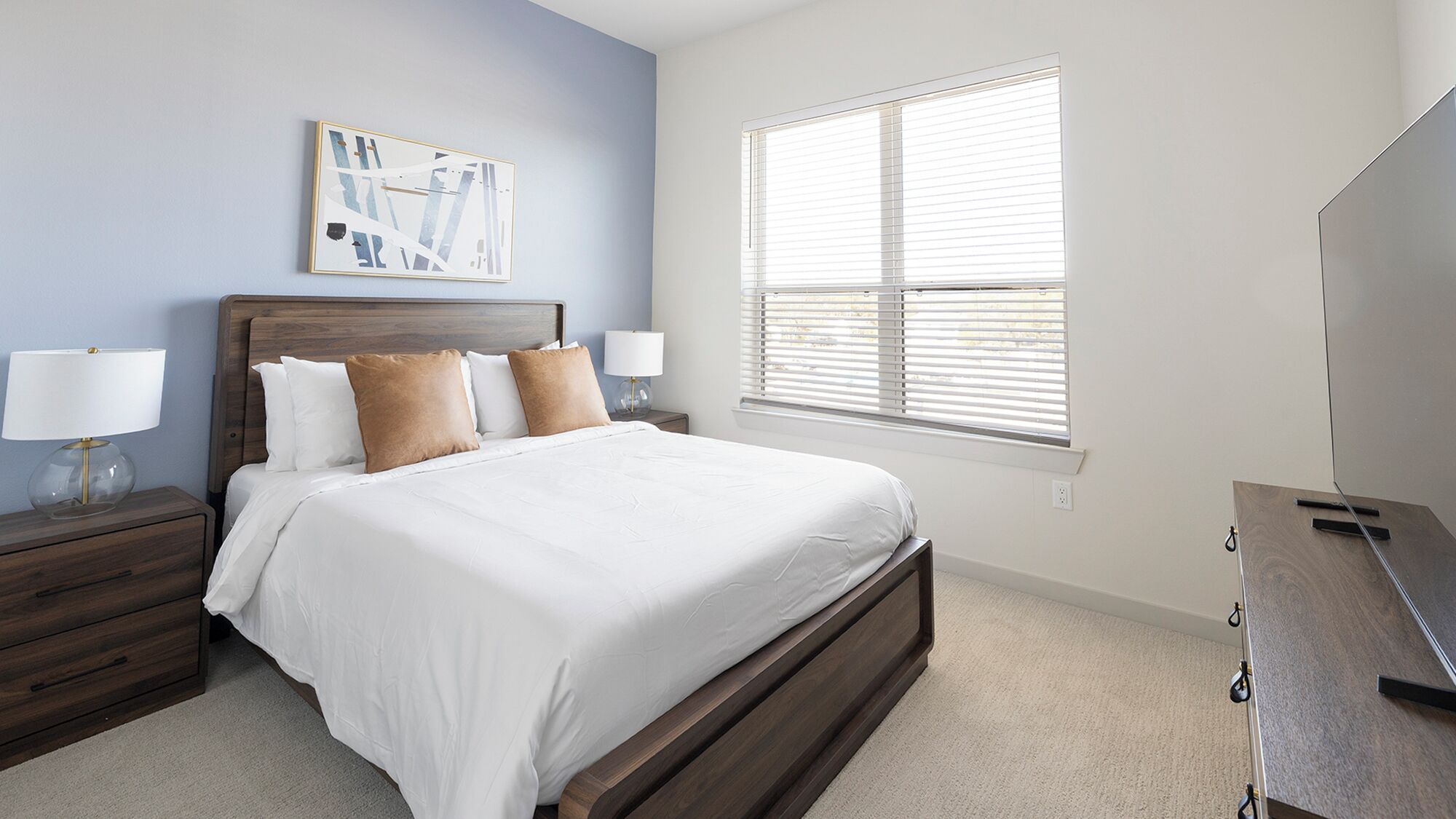 A bedroom with a bed, nightstands, a lamp, a dresser, a window with blinds, and a wall art piece.