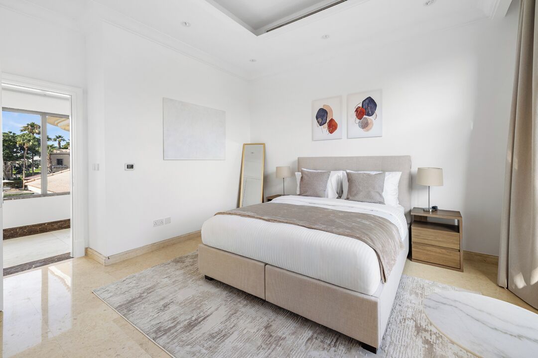 A modern bedroom with a large bed, a nightstand, and a view of the outdoors.