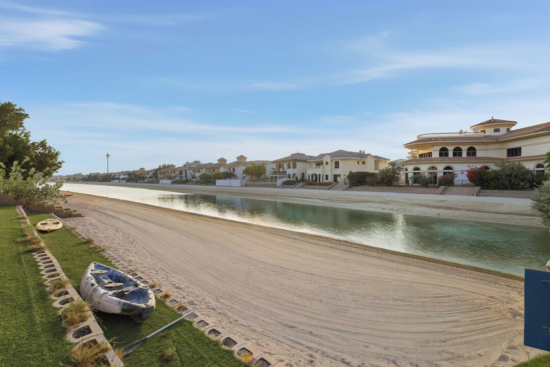 A riverfront property with a boat dock, a sandy beach, and a row of houses with Mediterranean architecture.