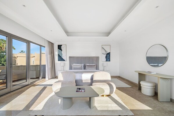 Et moderne soveværelse med en stor seng, et siddeområde og en balkon med skydedøre.