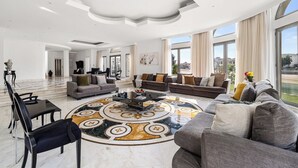Uma sala de estar ampla com uma grande mesa de centro redonda, vários sofás e piso de mármore.