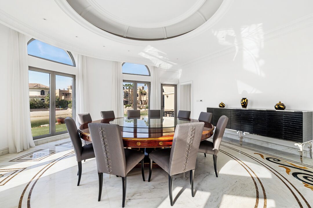 A spacious dining area with a round glass table surrounded by chairs, a black console table, and a view of the outdoors.