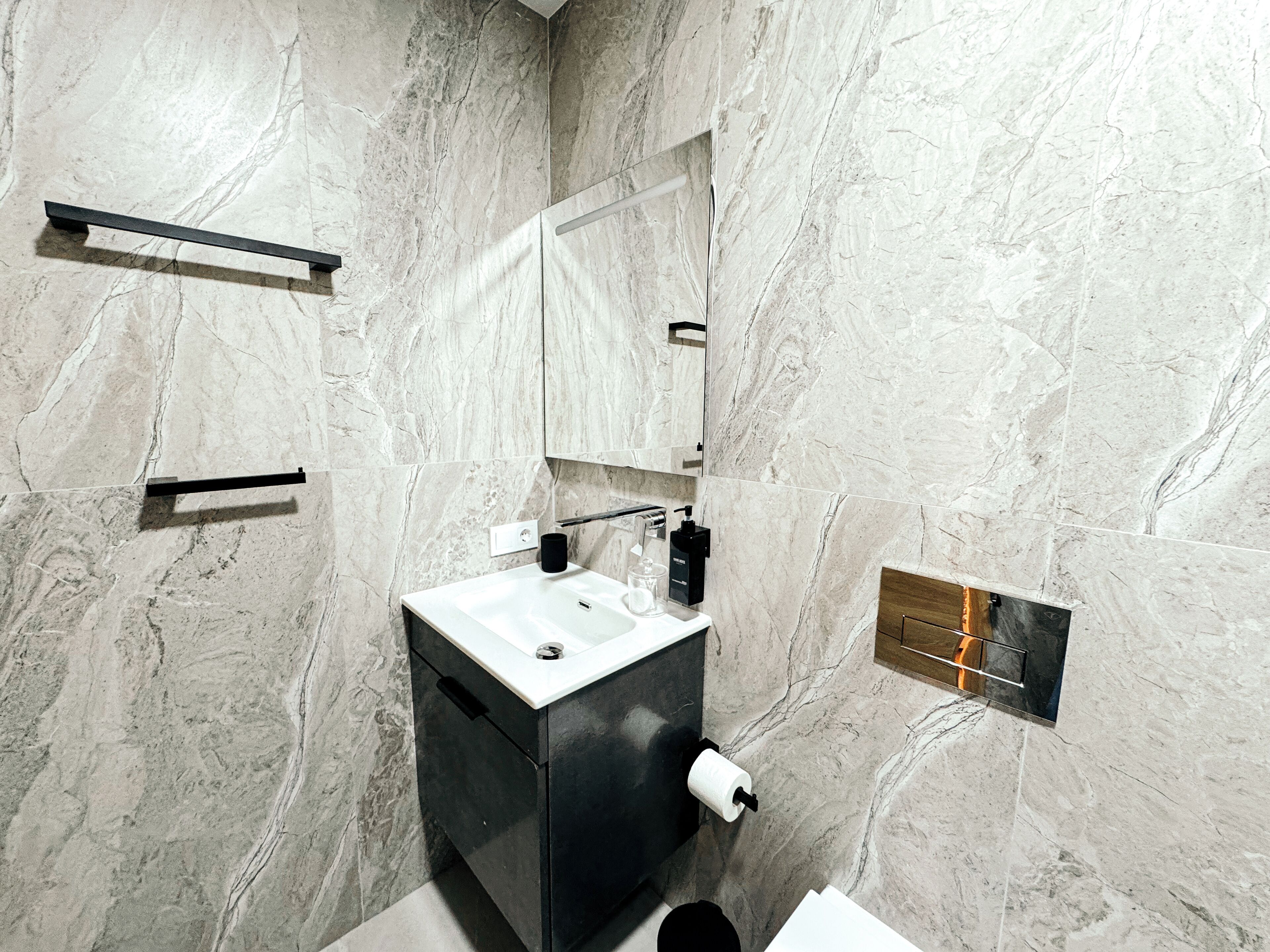 Une salle de bain moderne avec un mur en marbre, un lavabo noir, un miroir et un porte-serviettes.