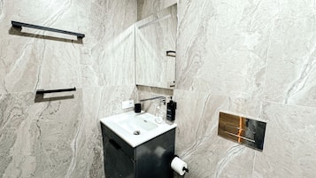 Une salle de bain moderne avec un mur en marbre, un lavabo noir, un miroir et un porte-serviettes.