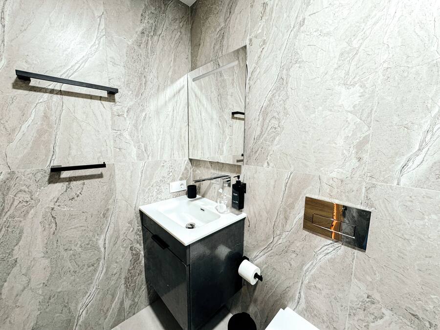 Une salle de bain moderne avec un mur en marbre, un lavabo noir, un miroir et un porte-serviettes.