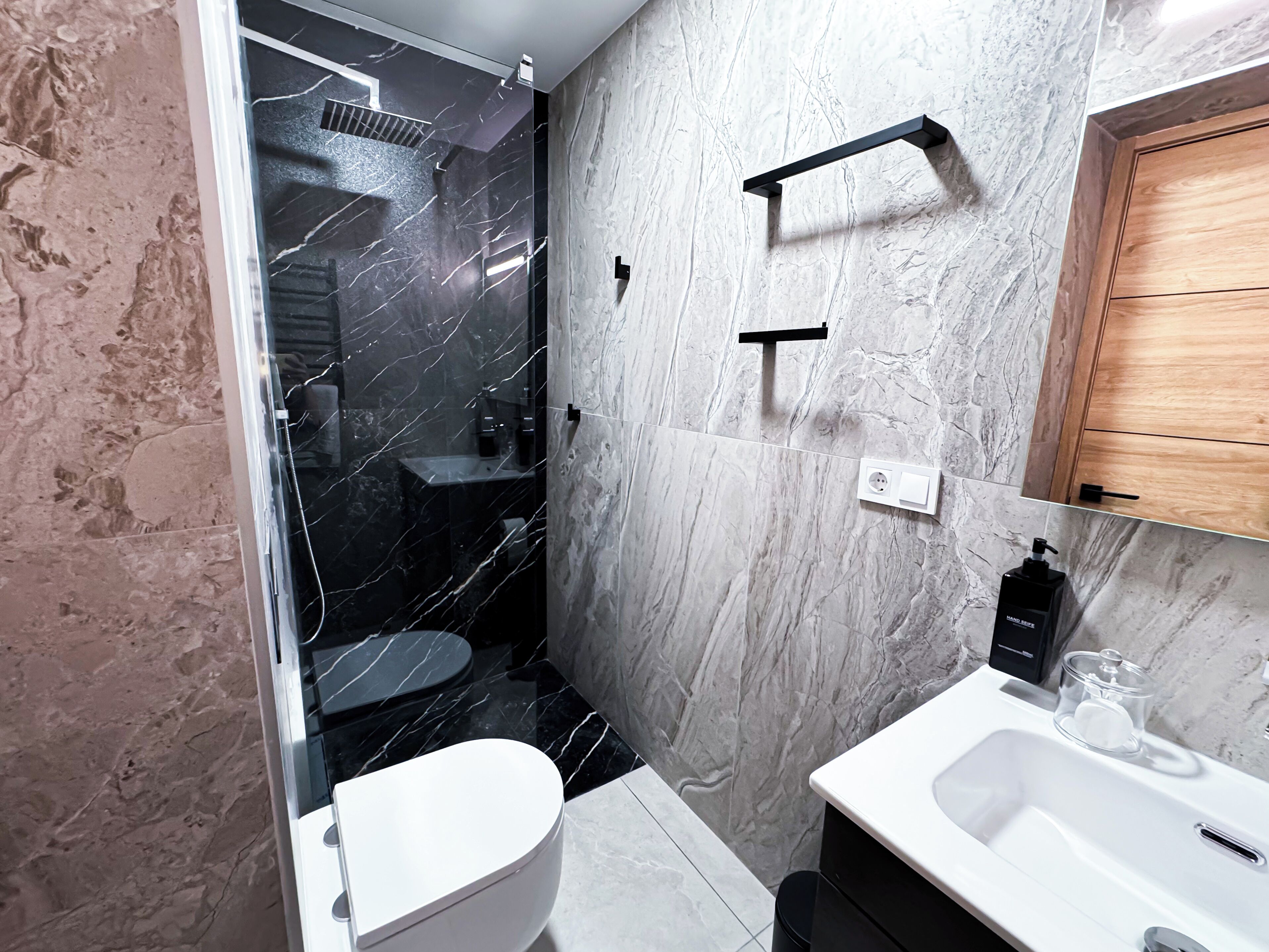 Et moderne badeværelse med toilet, håndvask og bruseområde.