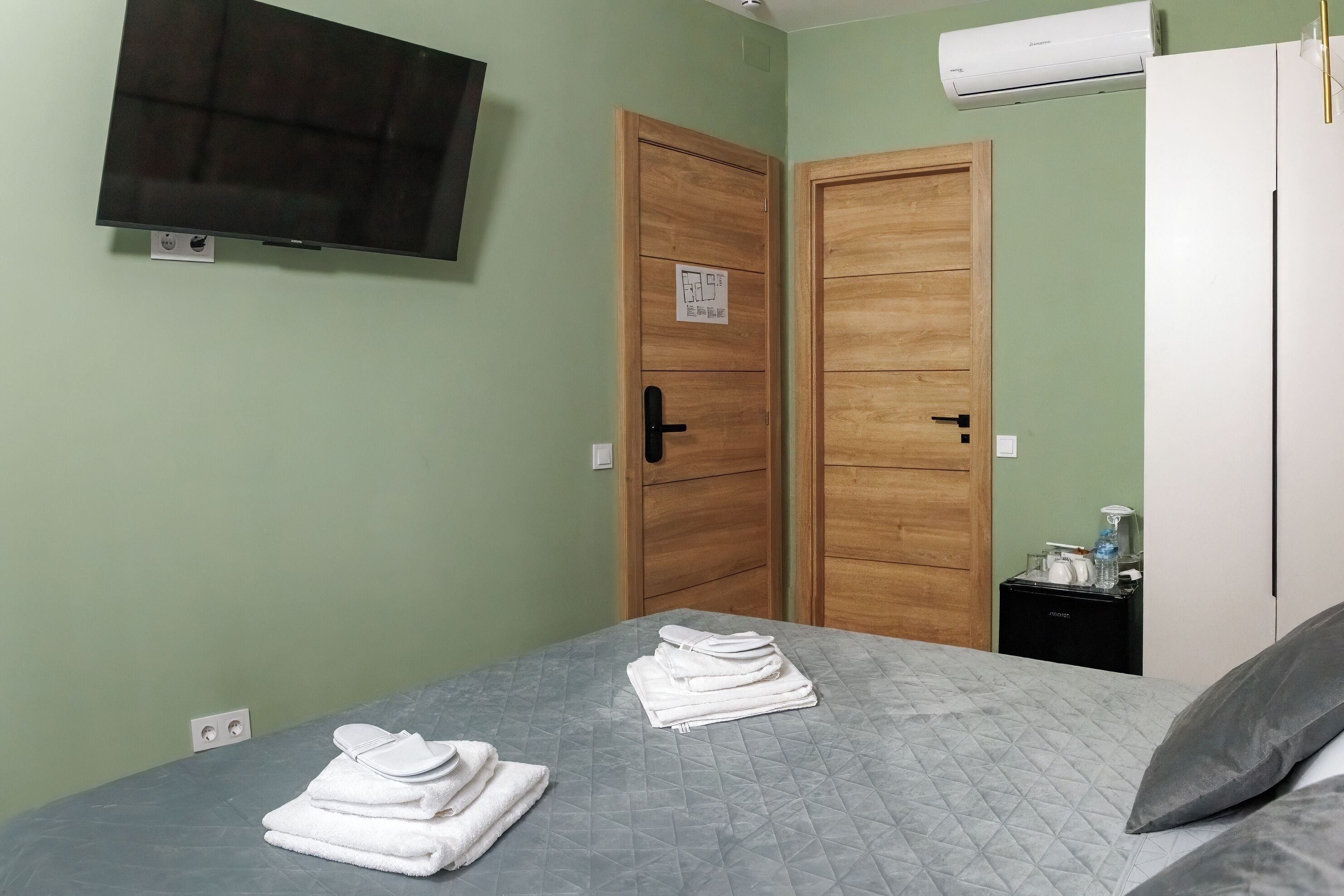 Una habitación con una cama, dos puertas de madera, un televisor y aire acondicionado.