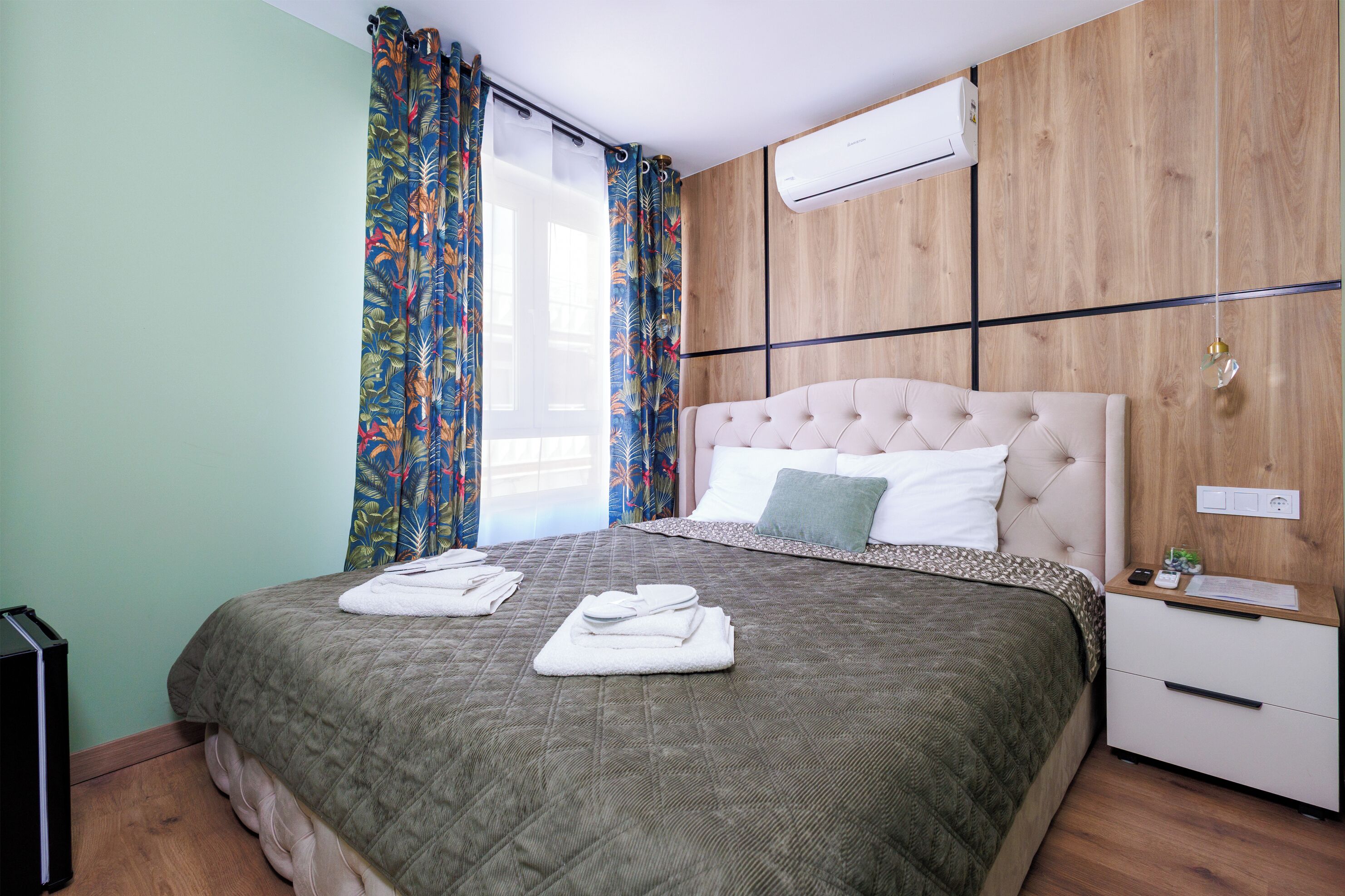 A neatly made bed with a quilted bedspread, a bedside table with a lamp, and a wall-mounted air conditioner.
