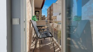 Un balcone con due sedie, un tavolino, una porta e vista sugli edifici.