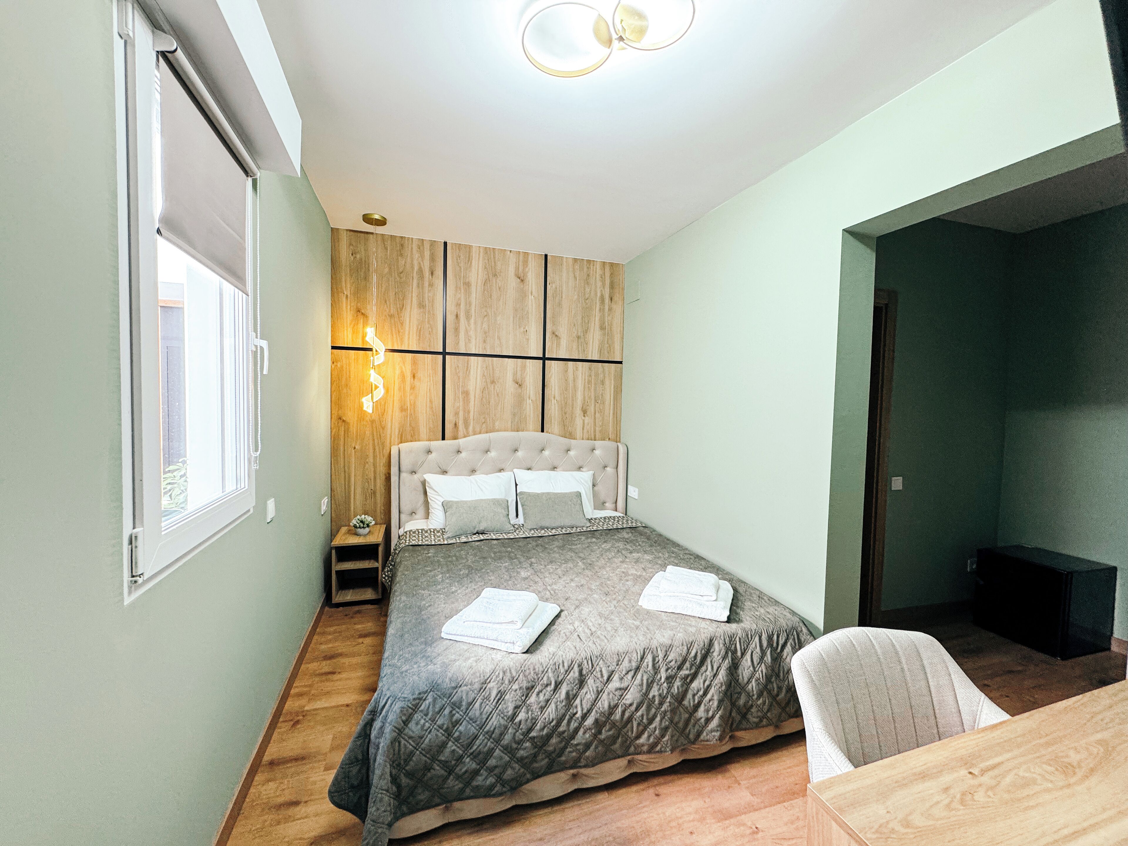 Un dormitorio con una cama, una mesita de noche pequeña, una silla y un panel de pared de madera.