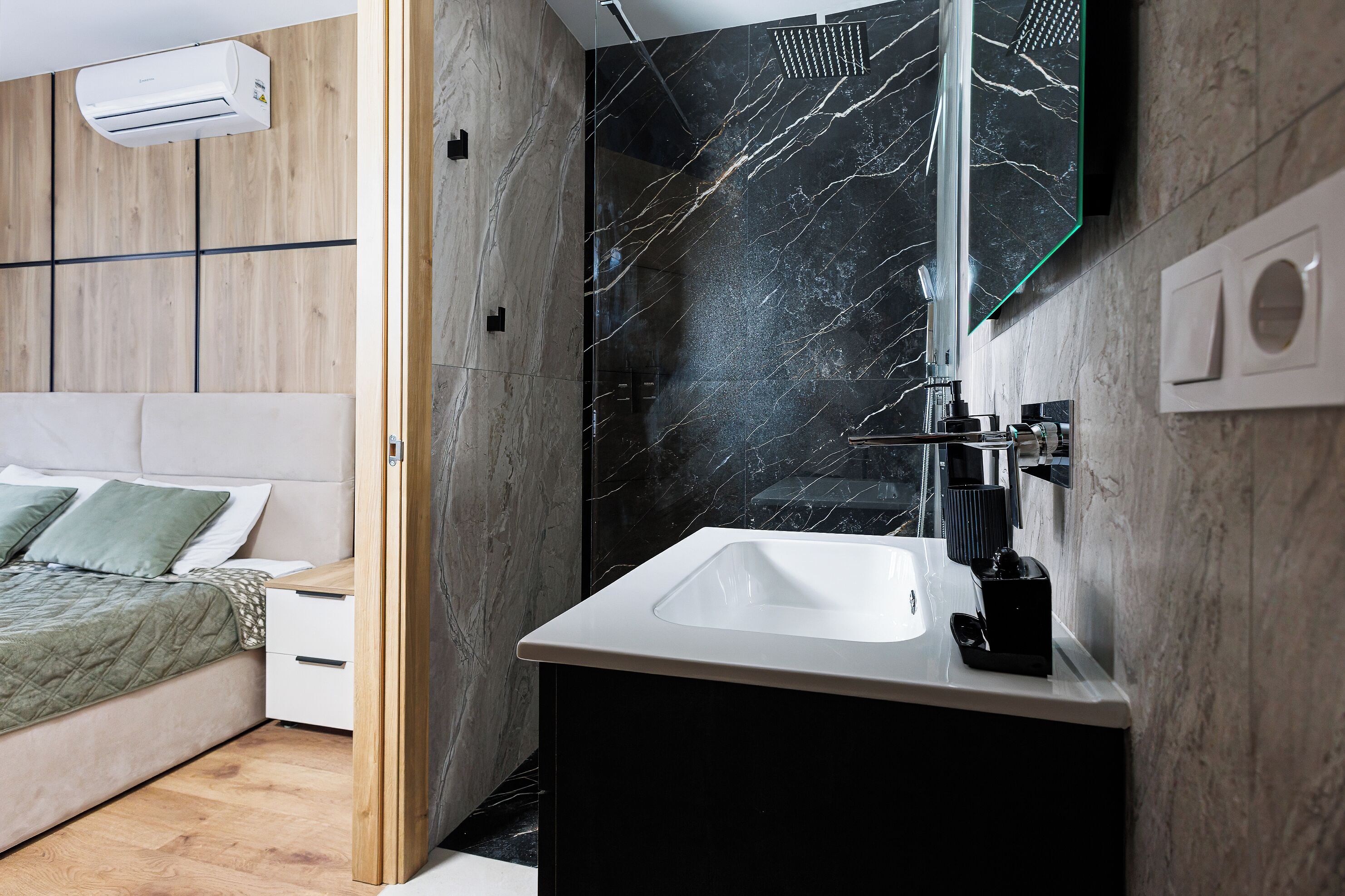Un baño moderno con pared de mármol negro, lavamanos blanco y cabina de ducha de vidrio.