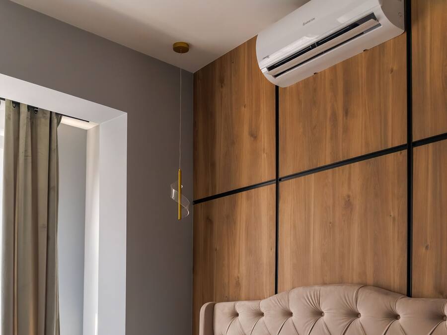 Habitació amb finestra, aire condicionat, llum penjada a la paret i capçal de llit amb textura.