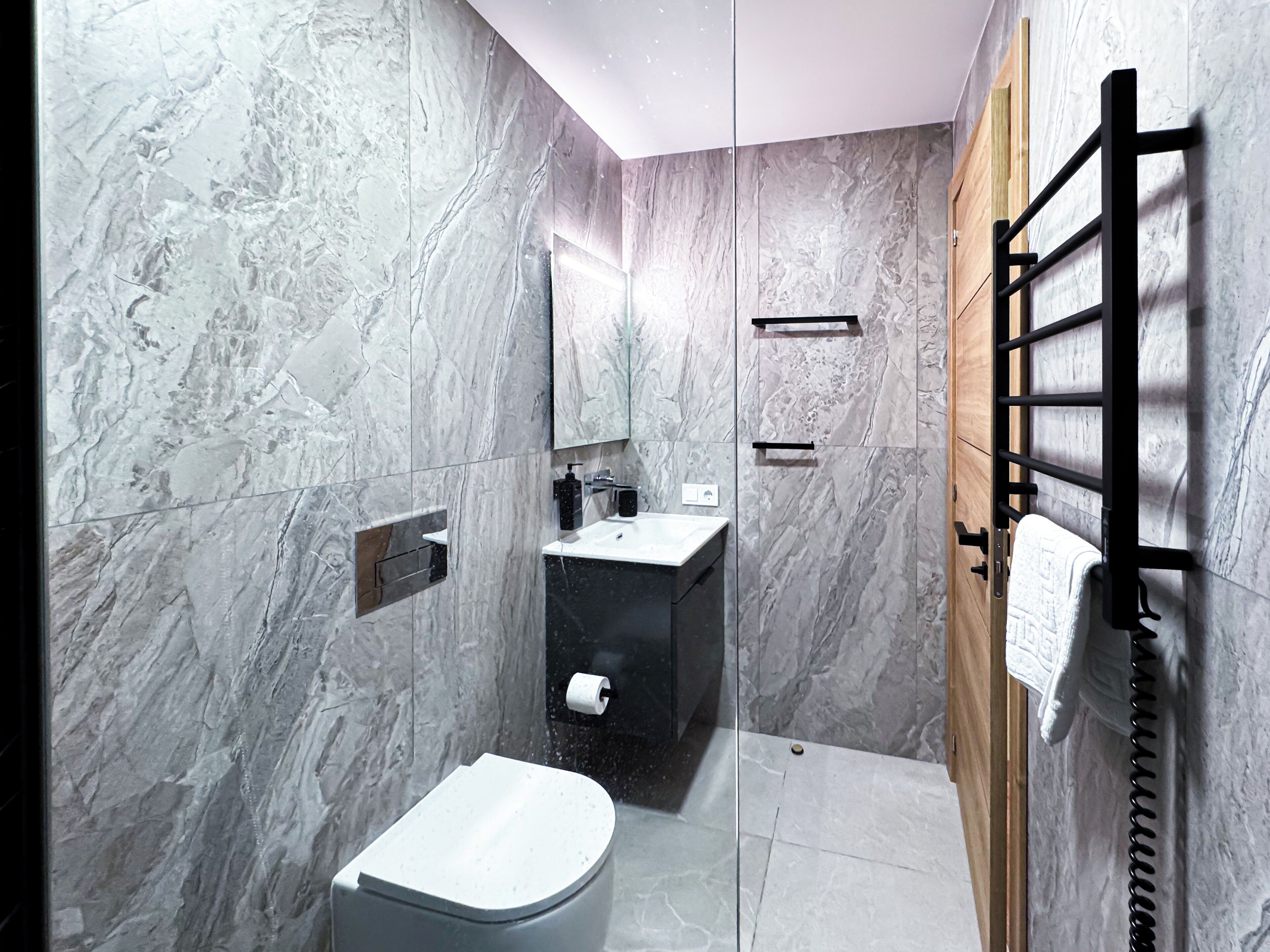 Une salle de bain moderne avec des murs en marbre, des toilettes, un lavabo et un porte-serviettes.