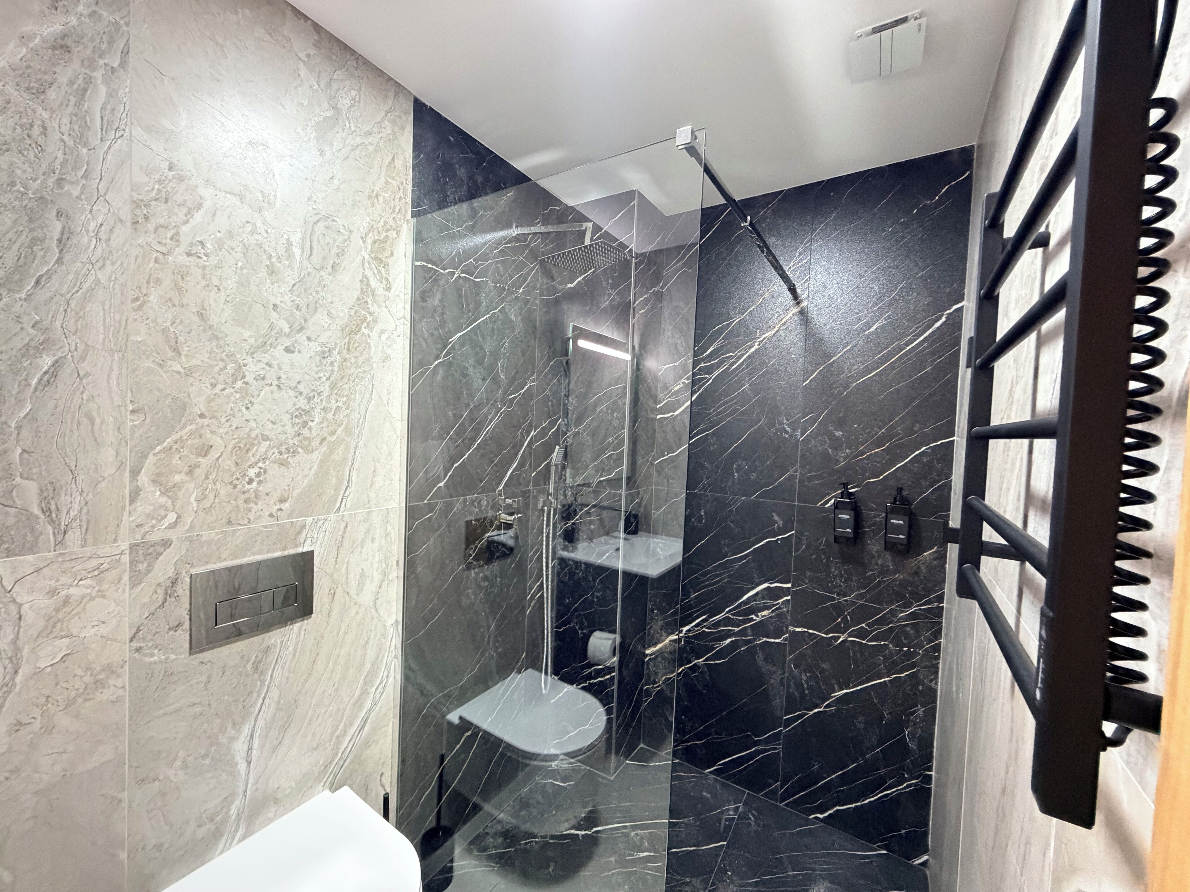 Un baño moderno con ducha envuelta en vidrio, paredes de mármol y una pared decorativa de mármol negro.