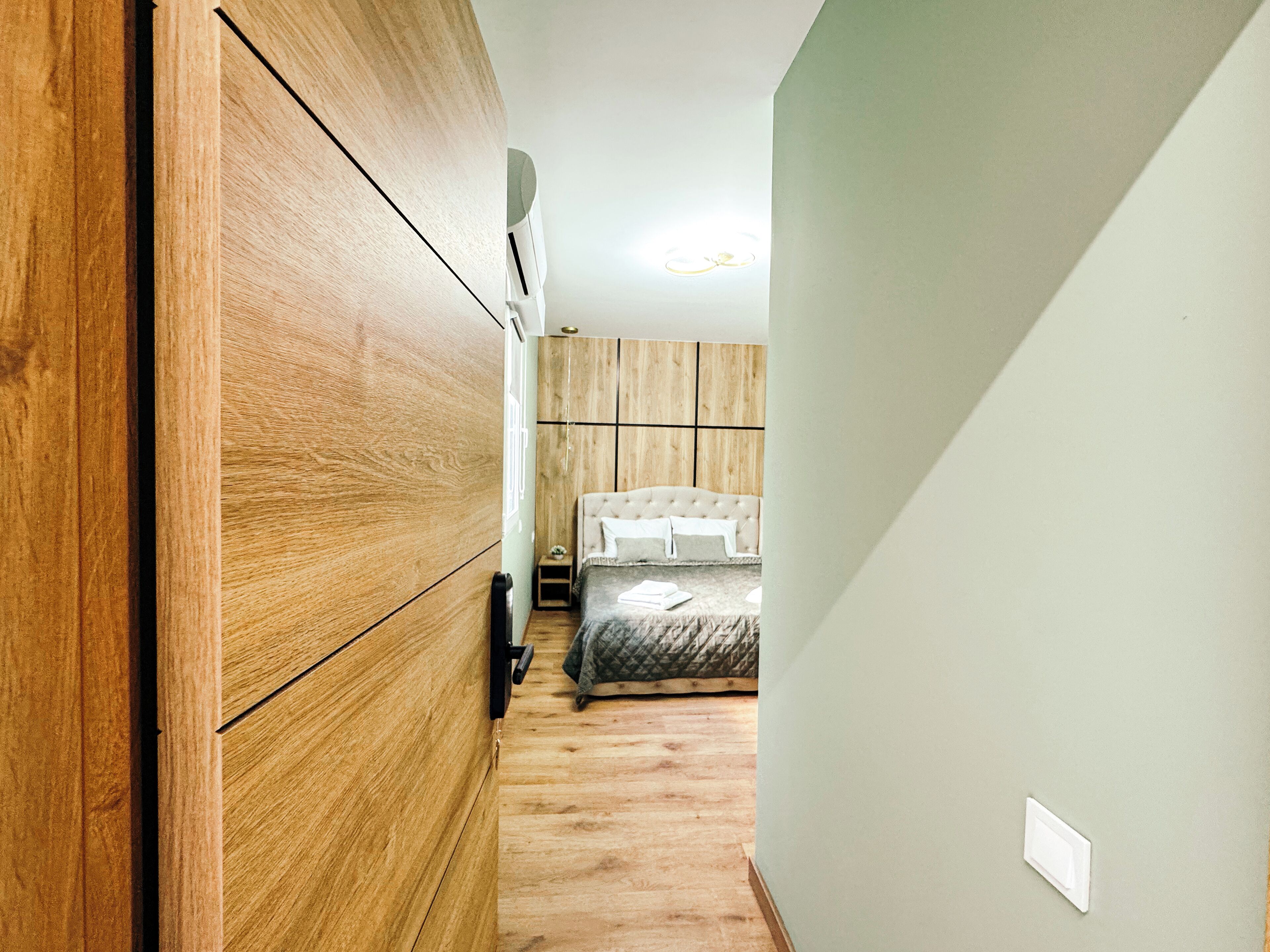 Quarto com guarda-roupa de madeira, cama com cobertura acolchoada e mesa de cabeceira com abajur.