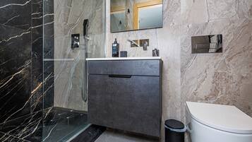 Une salle de bain avec un mur en marbre, un lavabo avec un miroir, des toilettes et une poubelle.