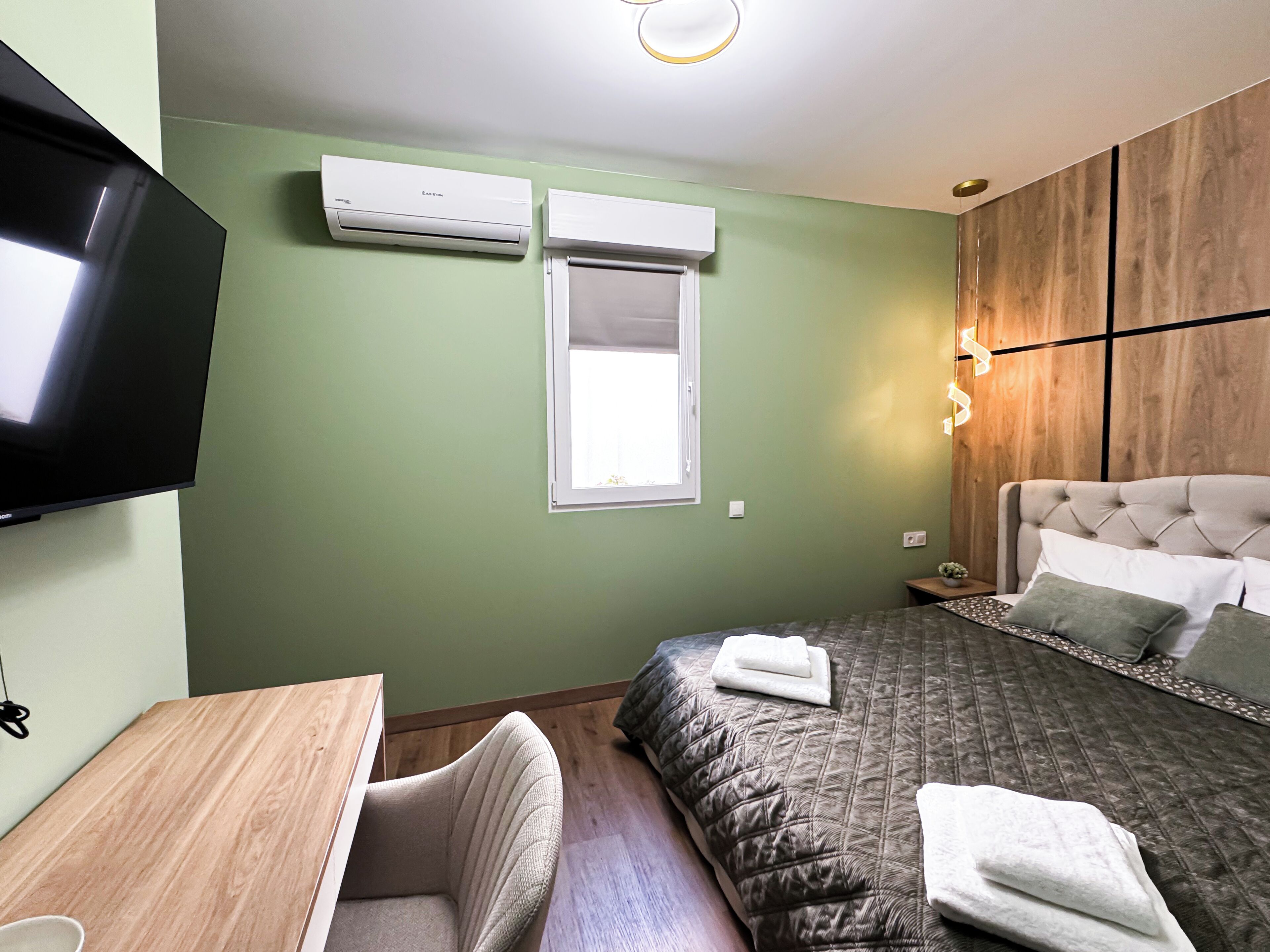Un dormitorio con cama, televisión, ventana y aire acondicionado.