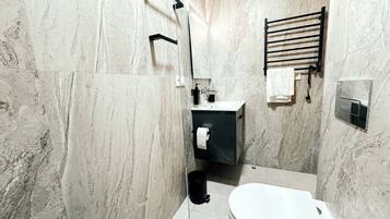 Un baño moderno con pared de mármol, un perchero negro, un inodoro y un lavabo con espejo.