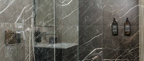 A bathroom with a glass-enclosed shower, a marble wall, and two toiletries on the wall.
